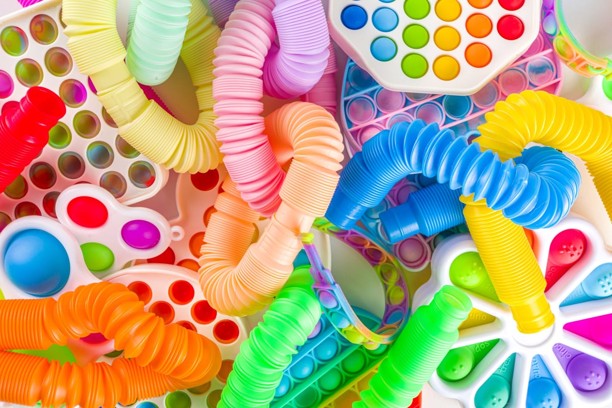 A bright set of kids fidget toys including pop-its and squishies laid out on a white surface