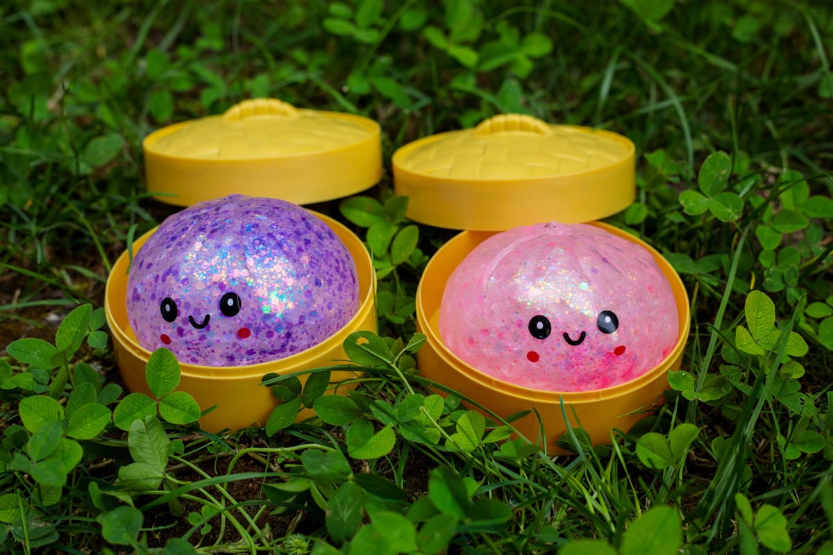 Glitter squishy dumpling toys in purple and pink sitting in open yellow steamer containers
