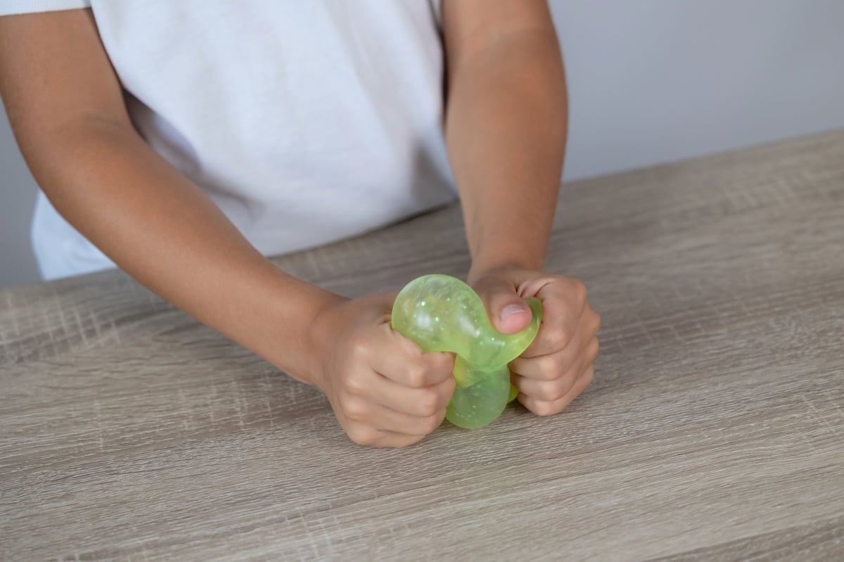 Close-up of a child's hands squeezing a translucent green stress toy on a wooden table