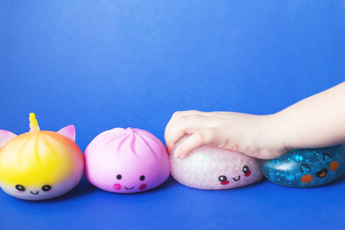 A child's hand squeezing a cute squishy toy during sensory play on a blue background